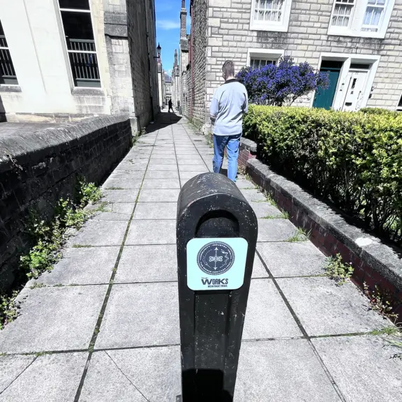 The Works Heritage Trail funded by Historic England and others. A vistior walking down a Railway Village alleyway showing use of an existing bollard as wayfinding